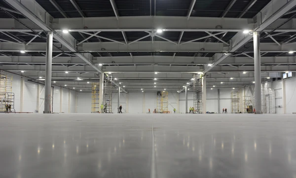 Vaste entrepôt industriel en cours d'aménagement avec ouvriers équipés d'échafaudages mobiles effectuant des travaux d'installation
